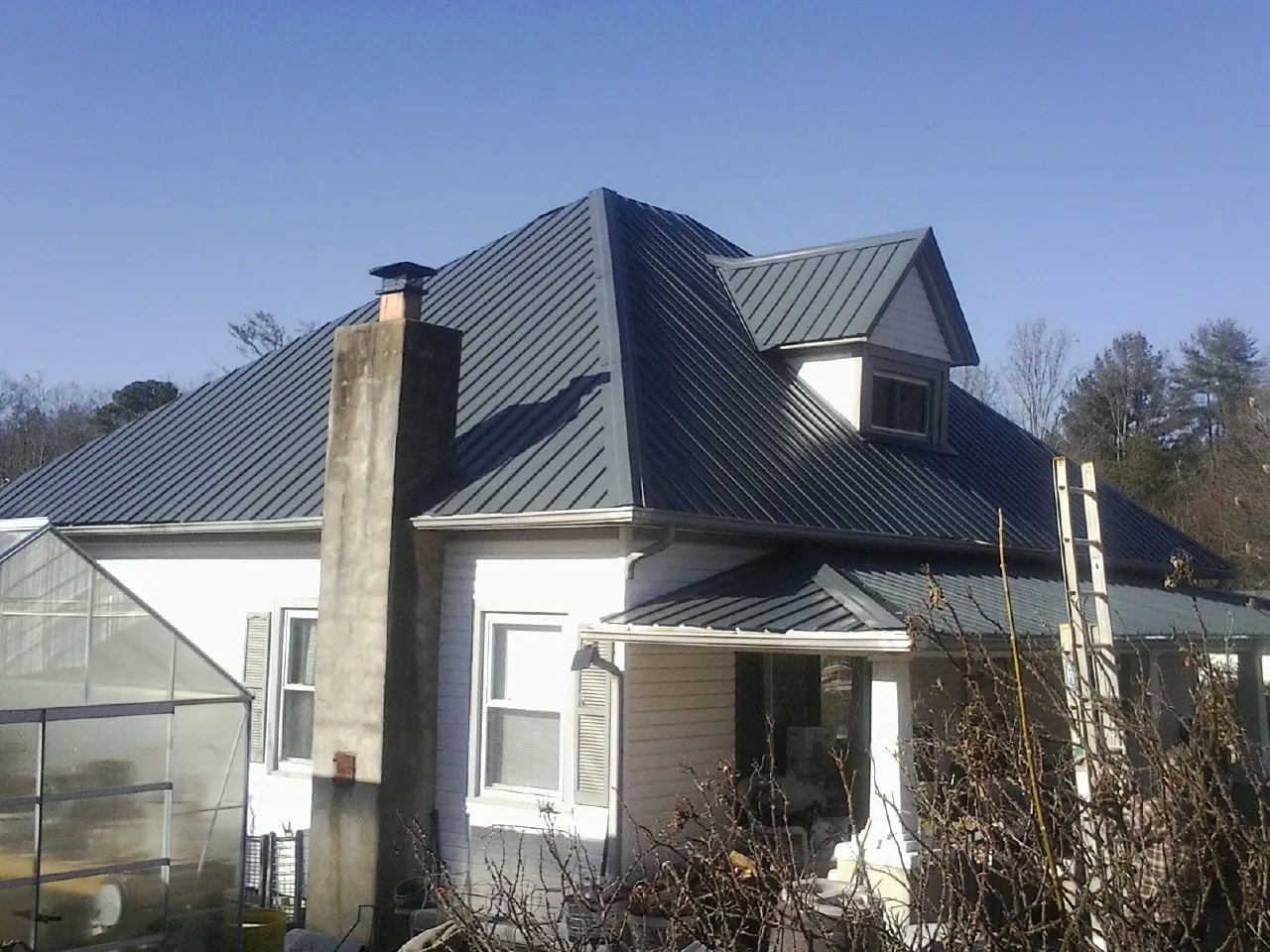 Dark blue standing seam metal roof on a white farmhouse with dormer — Slate & Tile Roof Repair by Roofing Brothers in Sunnyvale